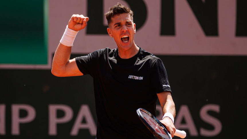 An Australian tennis player clenches his fist in celebration as he shouts with joy after winning a match at the French Open.