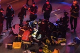 A woman is treated for injuries on the ground at night as a group of emergency workers surround her.
