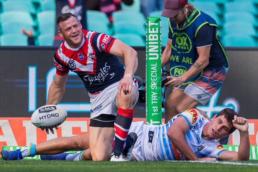 An kneeling NRL player gets ready to throw the ball away after scoring a try.