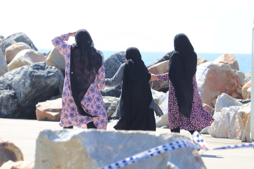 Three women walk on a beach hand in hand