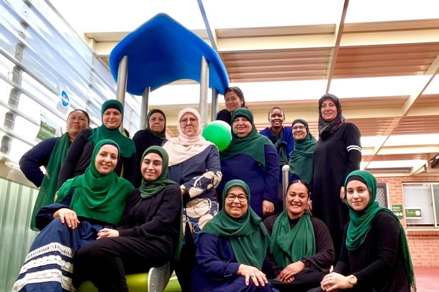 A group of women stand together in a group, smiling at the camera. 