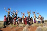 Eleven women, the Tjampi Desert Weavers, stand with their artworks, the Seven Sisters figures.