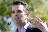 Donald Trump Jr speaks in the sunshine with trees blurred behind him