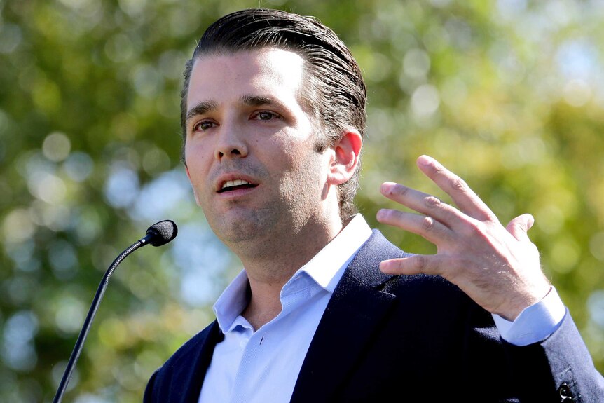 Donald Trump Jr speaks in the sunshine with trees blurred behind him