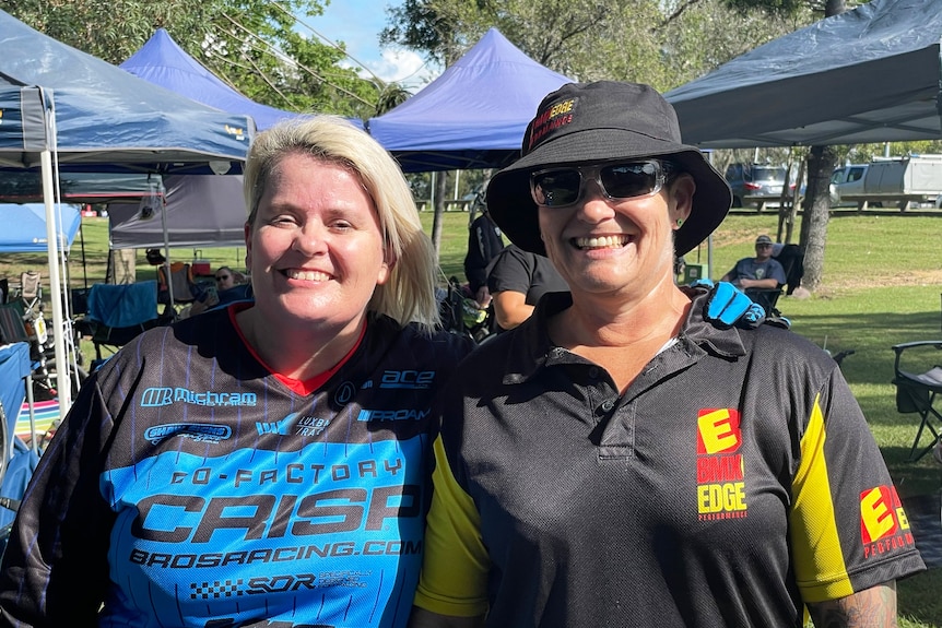 Raylene Pruett and Raina Beesley stand together outside at a BMX race meet.