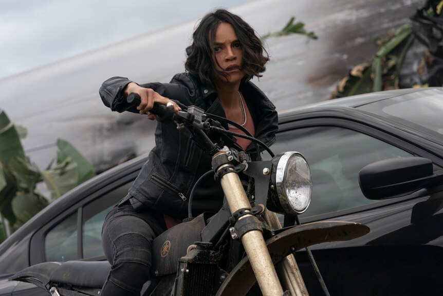 Michelle Rodriguez on a motorcycle, tensed forward, in Fast and Furious 9