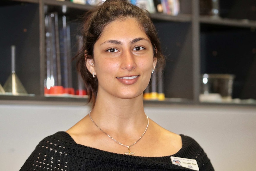 A head and shoulders shot of a female high school teacher posing for a photo in class and smiling.