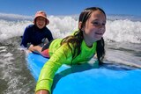 A girl and a woman catch a wave on a surfboard. 