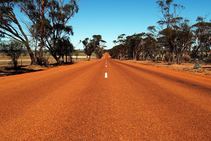 A long, straight stretch of red road in the Australian outback.