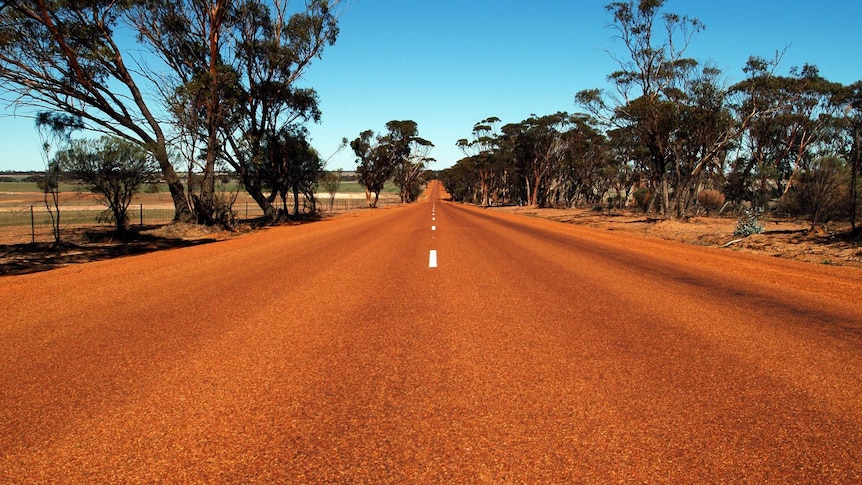 A long, straight stretch of red road in the Australian outback.