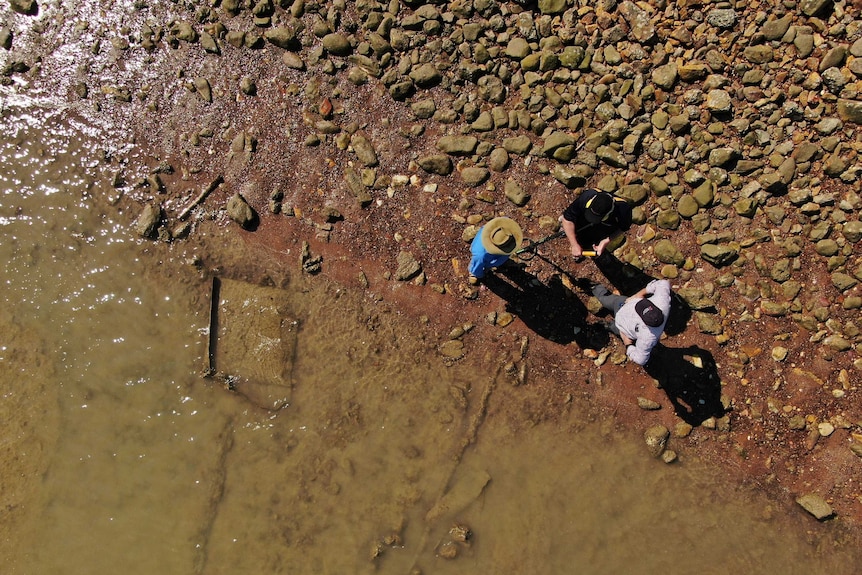 A drone photo of three people taking by the water, a cable can be seen entering the water.
