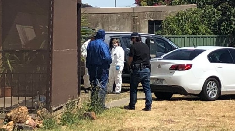 People in protective body suits with masks on stand around the entrance of a brick home.