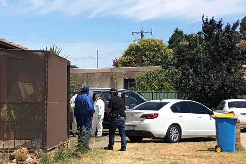 People in protective body suits with masks on stand around the entrance of a brick home.