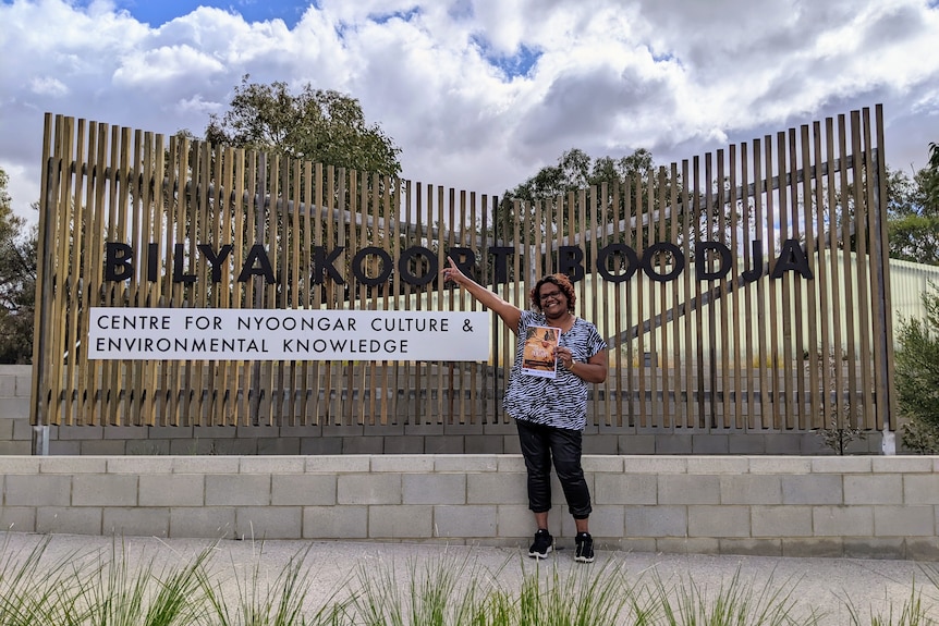 Smiling woman stands in front of the entrance sign for a cultural centre