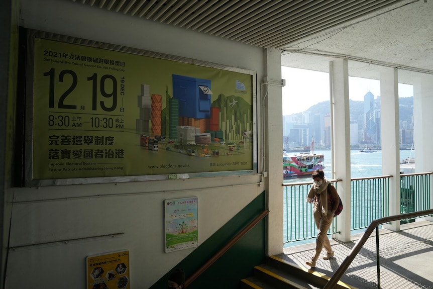 A woman walks towards a set of steps. On the wall beside her is a large banner with 12.19 written next to a ballot box graphic