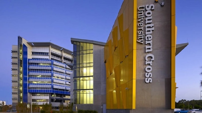 A large building with Southern Cross University written in white letters  on the side of the building at dusk