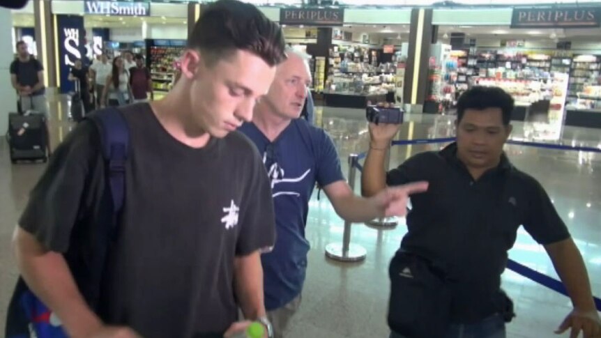 Jamie Murphy walks through an airport with his father and a man carrrying a video camera.