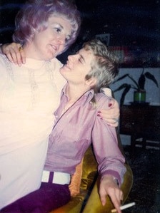 Perth brothel madam Shirley Finn stands with her arm around her then-girlfriend Rose Black who is sitting on a chair.