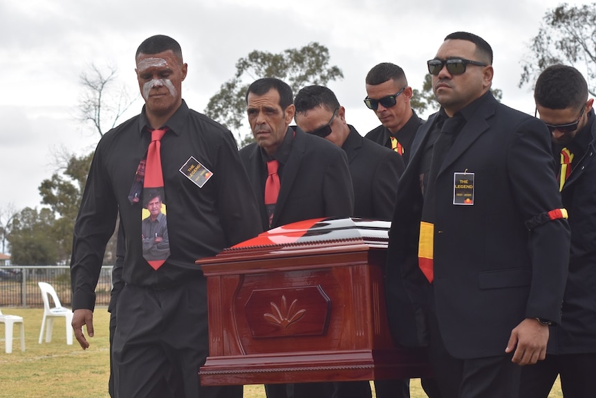 Pallbearers, wearing the Indigenous colours of black, red and yellow, carry a coffin