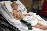Four-year-old boy lying in hospital bed looking at camera, leg bandaged.