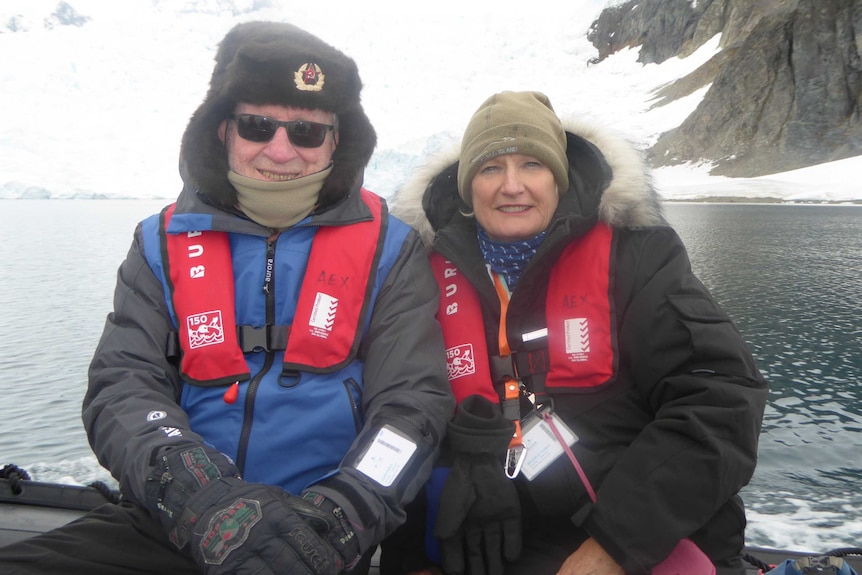 Bev and John Kable sit on a boat on water in front of ice and snow.