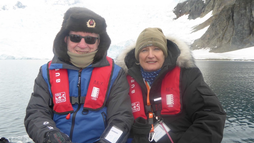 Bev and John Kable sit on a boat on water in front of ice and snow.