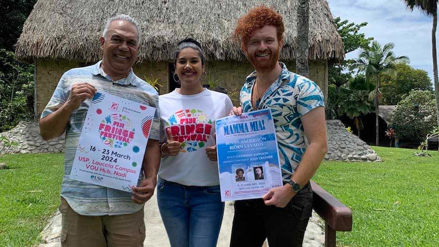 Three people hold a poster promoting the Mamma Mia! musical in Fiji