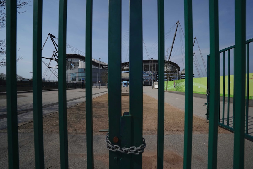 a green metal fence obscures the view of Etihad Stadium