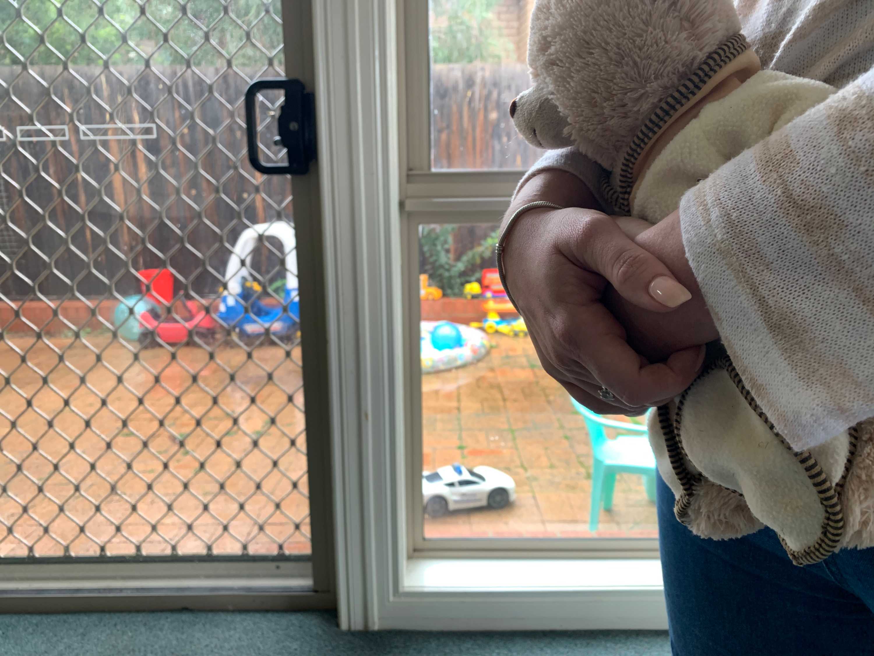A close-up of a woman&#x27;s hands holding a toy bear with children&#x27;s play equipment in the background.