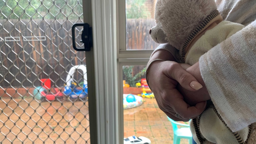 A close-up of a woman's hands holding a toy bear with children's play equipment in the background.