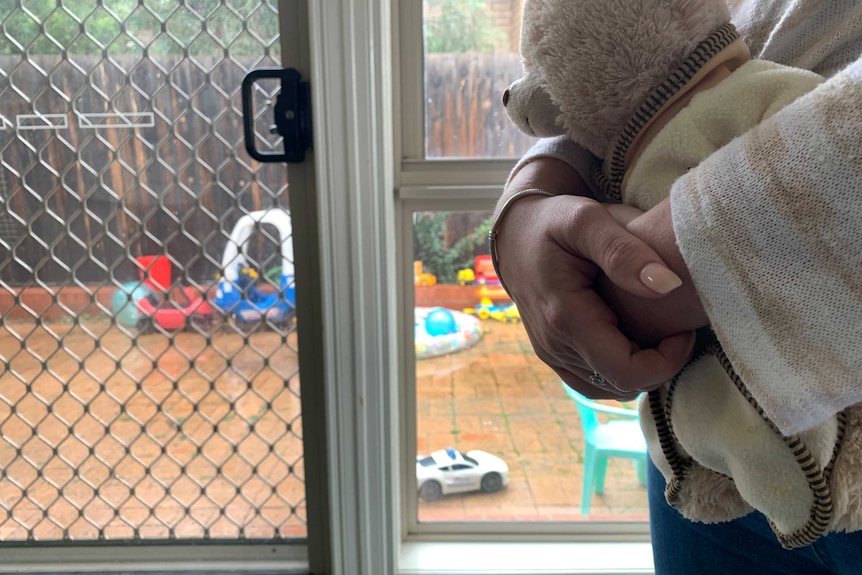 A close-up of a woman's hands holding a toy bear with children's play equipment in the background.