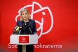 Sweden's Prime Minister Magdalena Andersson speaks from a podium in front of a red backdrop.