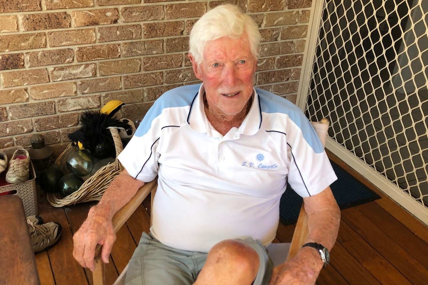 Man with white hit sits on back deck in polo shirt and casual shorts.