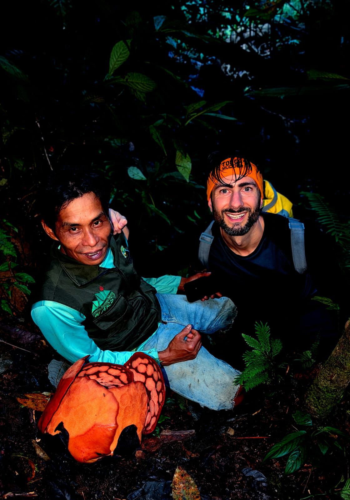 Two men smile in a darkened jungle.