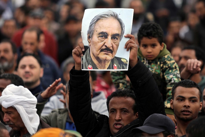 A man holds a poster of Eastern Libyan military commander Khalifa Haftar in a crowd of demonstrators.