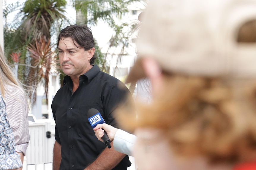 Celebrity crocodile wrangler Matt Wright walking along a footpath and looking serious, as a reporter points a microphone at him.