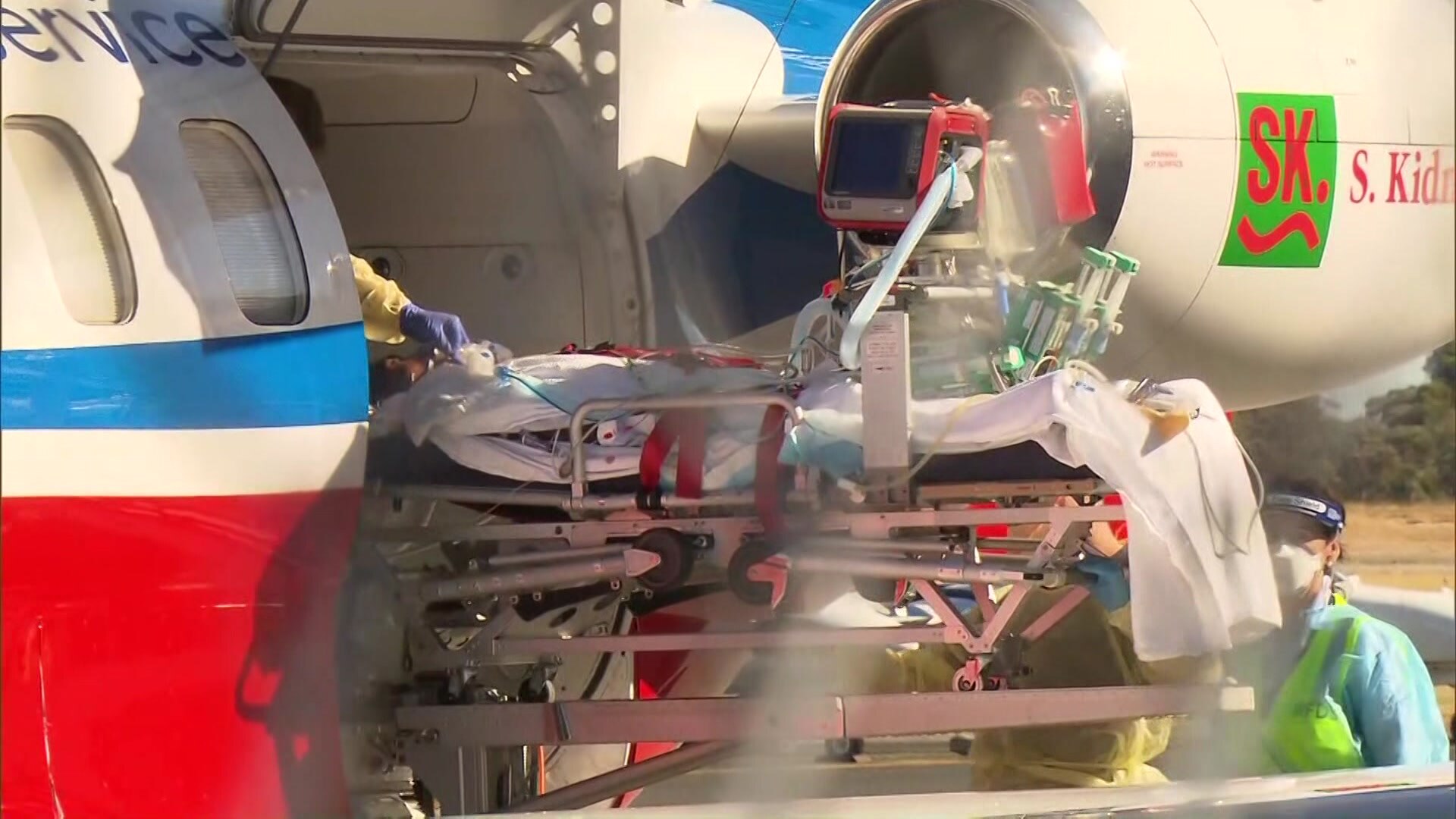 A man hooked up to medical gear being lifted off a helicopter