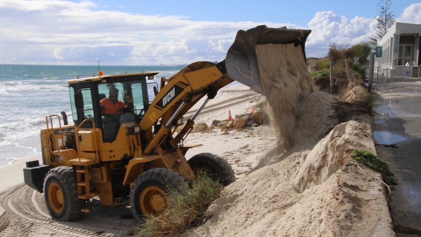 An excavator shores up sand on Port Beach after erosion from a storm.