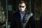 A man wearing sunglasses, a face mask and a puffer jacket