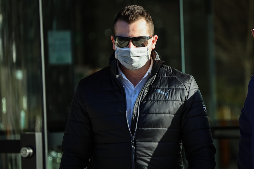 A man wearing sunglasses, a face mask and a puffer jacket