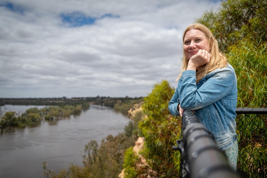 Yvette Kelly stands at a looking out at the river her head resting on her hand as she leans against a look-out fence