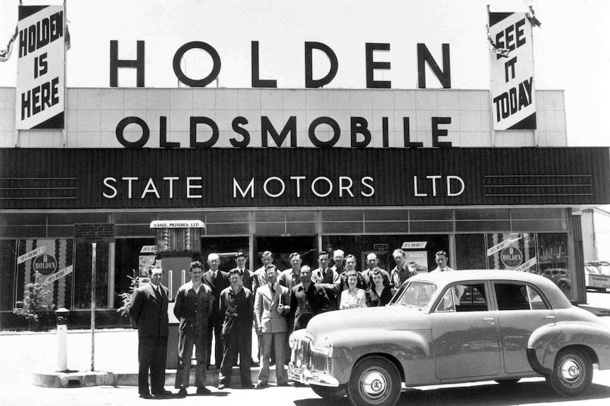Employees stand outside State Motors car yard with a Holden, in 1948