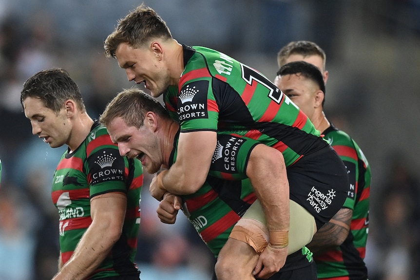 A South Sydney NRL player gives a teammate a piggy back ride as they celebrate a try.