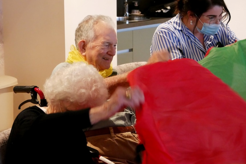 An elderly man helps to lift a silk parachute during a music class