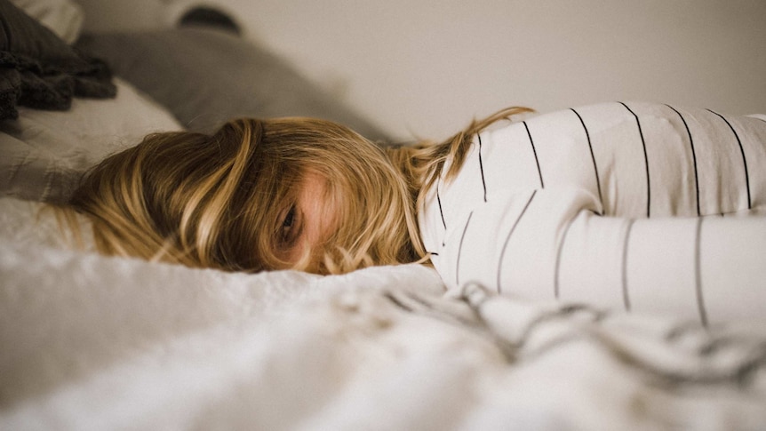 A woman with a pained expression lying face down on a pillow