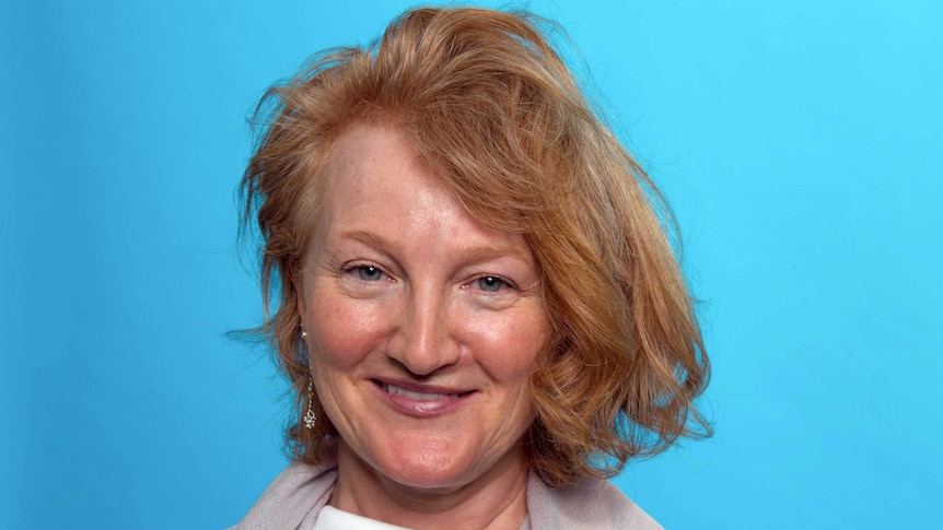 A portrait of radio maker Krista Tippett smiling against a sky blue background.