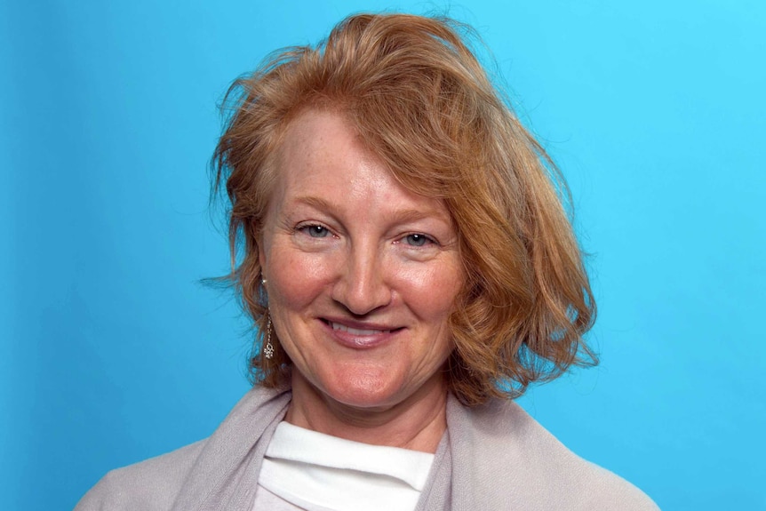 A portrait of radio maker Krista Tippett smiling against a sky blue background.