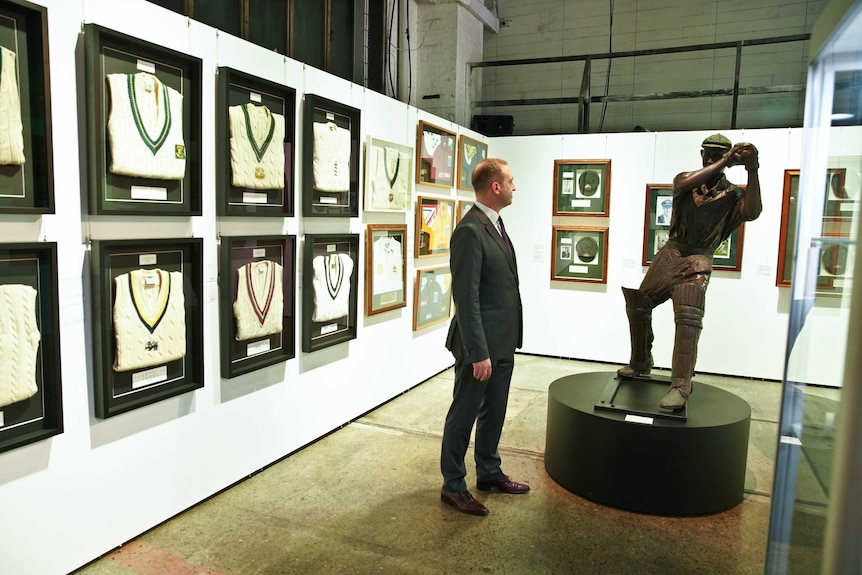 A man is seen standing in an exhibit hall surrounded by cricket items.