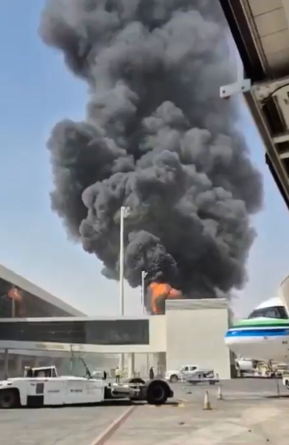 An blurry image in portrait shows a plume of smoke rising from behind an airport.