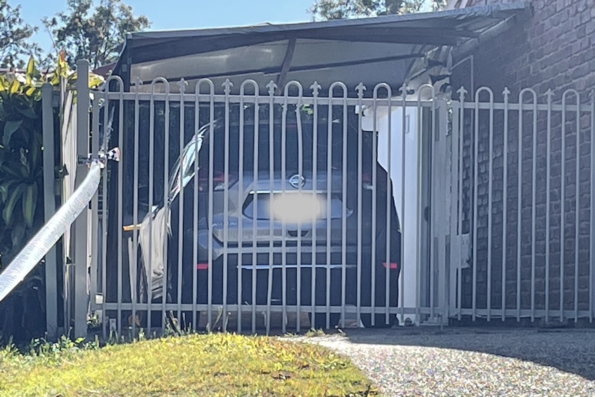 A grey car in a driveway behind a fence.